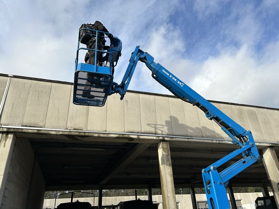 Deskundige in een hoogwerker inspecteert de dakrand van een gebouw