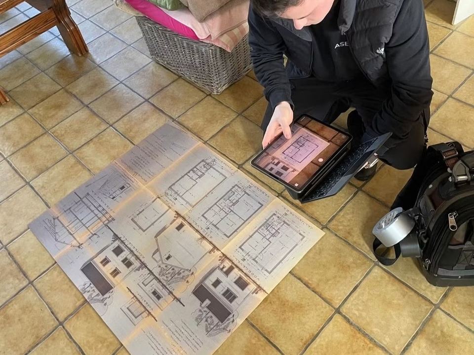 Deskundige fotografeert een oud bouwplan met een tablet tijdens het plaatsbezoek